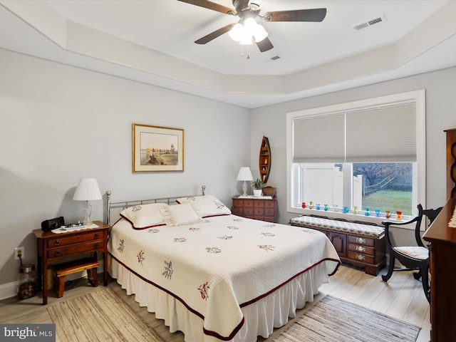 bedroom with ceiling fan, a raised ceiling, and light wood-type flooring