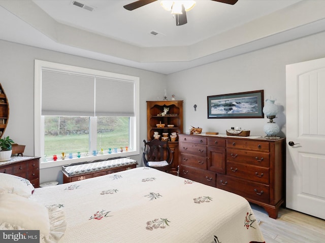 bedroom featuring light hardwood / wood-style flooring, a raised ceiling, and ceiling fan