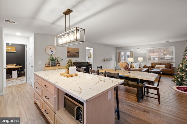 kitchen with a breakfast bar area, light brown cabinetry, light hardwood / wood-style flooring, and hanging light fixtures