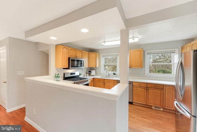 kitchen featuring kitchen peninsula, light wood-type flooring, appliances with stainless steel finishes, and sink