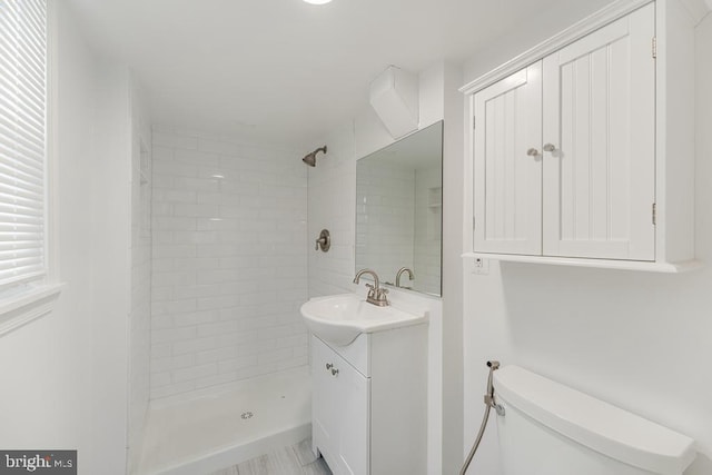 bathroom featuring toilet, a tile shower, and vanity