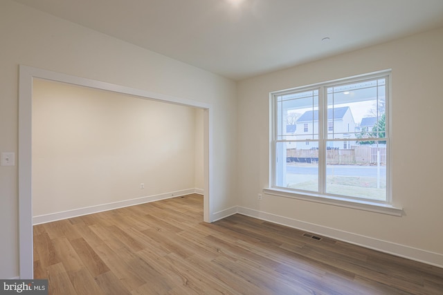 unfurnished room with wood finished floors, visible vents, and baseboards