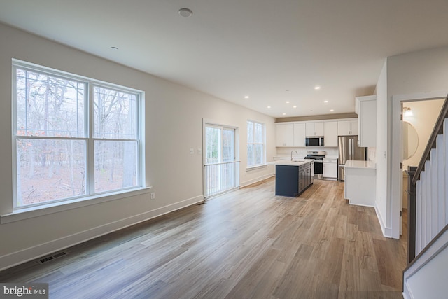 kitchen featuring light countertops, visible vents, appliances with stainless steel finishes, white cabinetry, and a kitchen island with sink