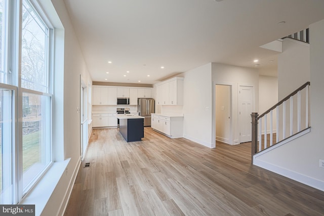 kitchen featuring white cabinets, light wood-style flooring, appliances with stainless steel finishes, a center island, and light countertops