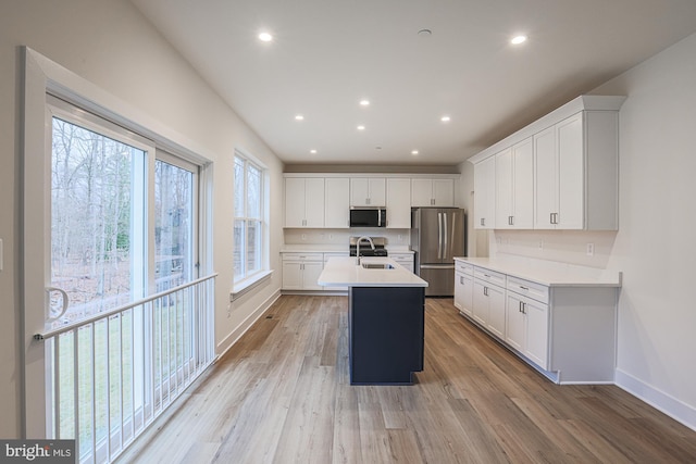 kitchen featuring an island with sink, appliances with stainless steel finishes, light countertops, light wood-type flooring, and a sink