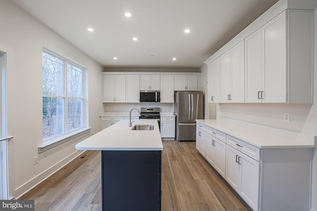 kitchen with appliances with stainless steel finishes, light countertops, light wood-type flooring, a sink, and recessed lighting