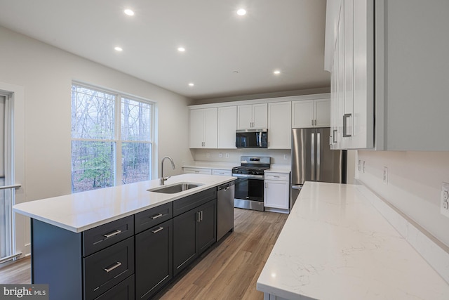 kitchen with a center island with sink, white cabinets, appliances with stainless steel finishes, light wood-type flooring, and a sink