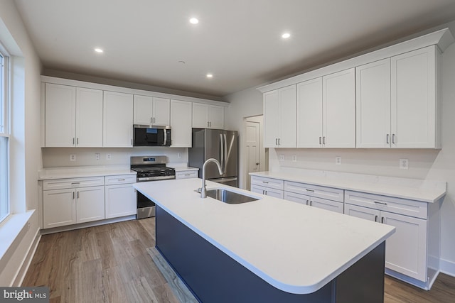 kitchen with appliances with stainless steel finishes, a sink, a center island with sink, and white cabinets