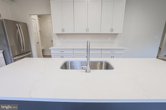 kitchen featuring light stone countertops, white cabinets, a sink, and freestanding refrigerator