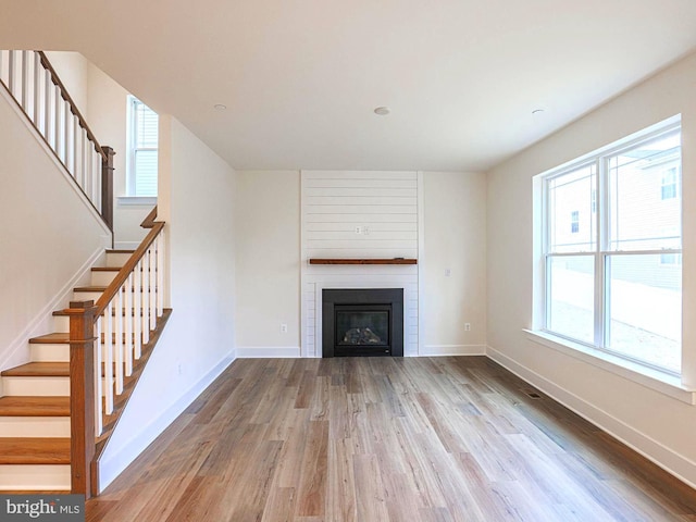 unfurnished living room featuring stairway, a fireplace, baseboards, and wood finished floors