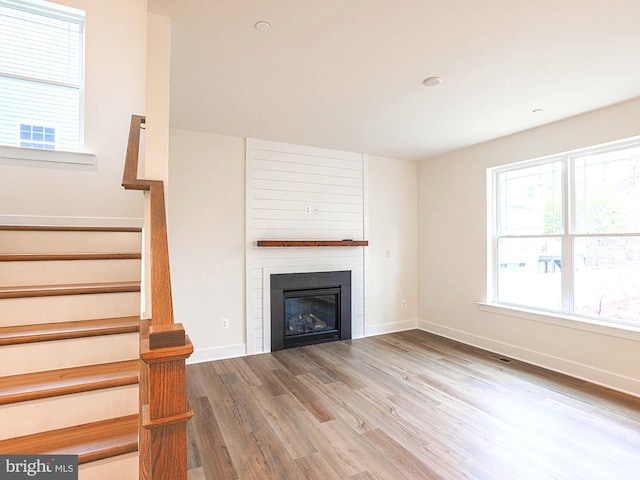 unfurnished living room featuring a large fireplace, wood finished floors, visible vents, baseboards, and stairway