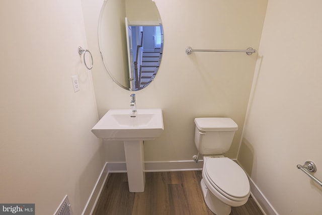 half bath with toilet, visible vents, baseboards, and wood finished floors