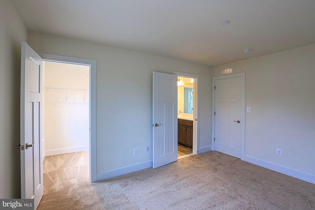 unfurnished bedroom with baseboards, a closet, a walk in closet, and light colored carpet