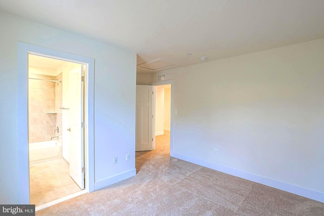 unfurnished bedroom featuring light carpet, ensuite bathroom, attic access, and baseboards