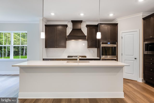 kitchen featuring hanging light fixtures, an island with sink, light hardwood / wood-style floors, and custom range hood