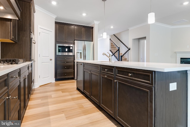 kitchen featuring appliances with stainless steel finishes, extractor fan, light hardwood / wood-style floors, a kitchen island, and hanging light fixtures