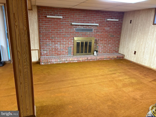 unfurnished living room featuring carpet, a paneled ceiling, a fireplace, and wooden walls