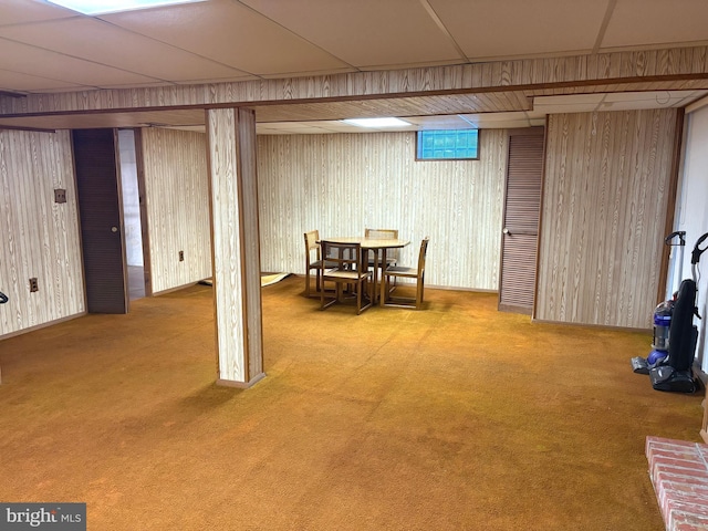 basement featuring carpet flooring, a drop ceiling, and wood walls