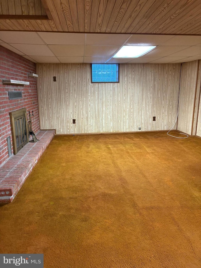 basement featuring carpet flooring, wooden walls, a drop ceiling, and a fireplace