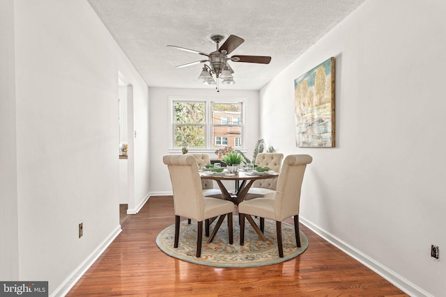 dining room with baseboards, a ceiling fan, a textured ceiling, and wood finished floors