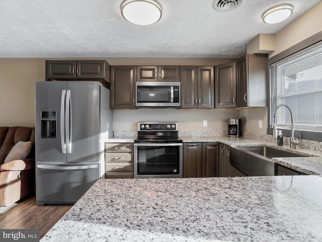 kitchen with dark brown cabinetry, light stone counters, sink, and appliances with stainless steel finishes