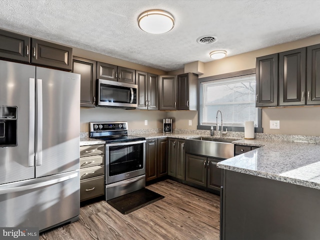 kitchen featuring appliances with stainless steel finishes, light stone counters, a textured ceiling, dark wood-type flooring, and sink