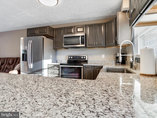 kitchen with light stone countertops, a textured ceiling, stainless steel appliances, dark brown cabinetry, and sink