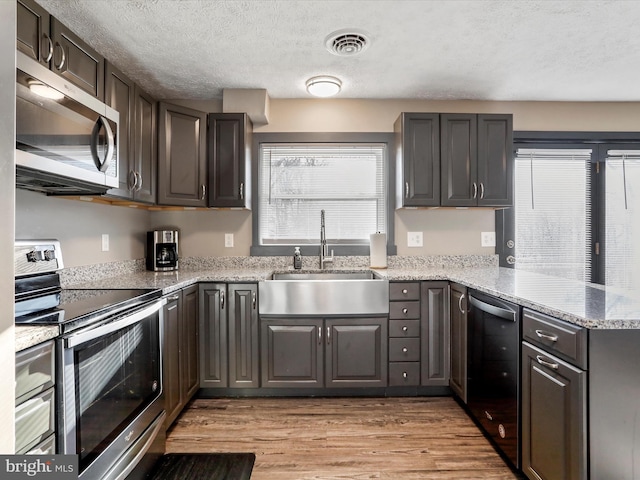 kitchen featuring sink, light hardwood / wood-style flooring, kitchen peninsula, a textured ceiling, and appliances with stainless steel finishes