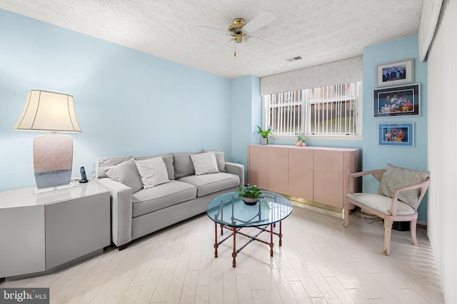 living room with ceiling fan, light hardwood / wood-style flooring, and a textured ceiling