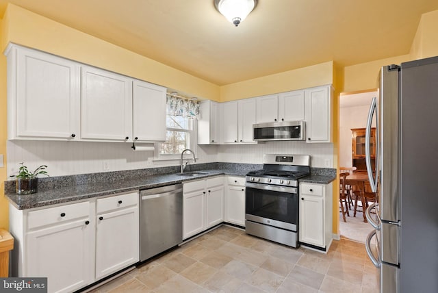 kitchen featuring appliances with stainless steel finishes, white cabinetry, dark stone countertops, and sink