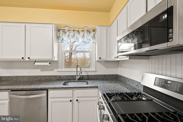 kitchen featuring dark stone counters, white cabinetry, sink, and stainless steel appliances