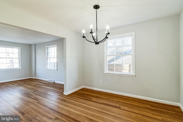 spare room with an inviting chandelier, visible vents, baseboards, and wood finished floors