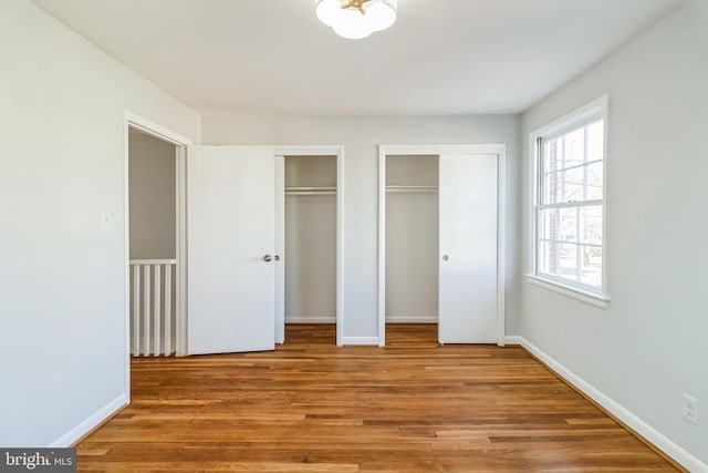 unfurnished bedroom with baseboards, light wood-type flooring, and multiple closets