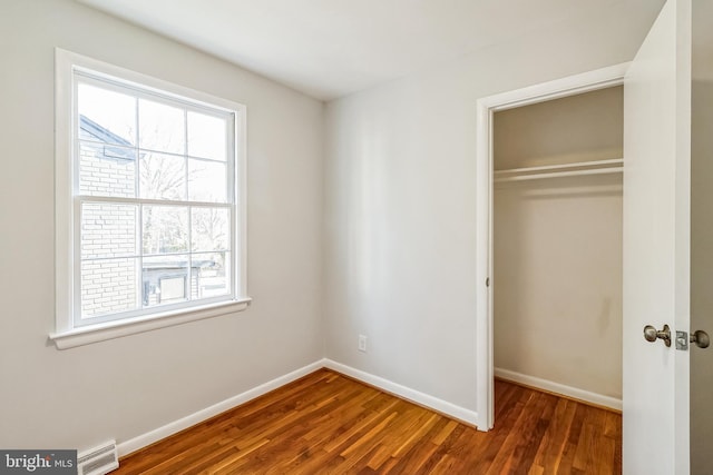 unfurnished bedroom with a closet, wood finished floors, visible vents, and baseboards