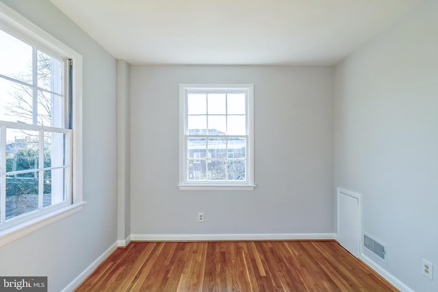 unfurnished room featuring wood finished floors, visible vents, and a healthy amount of sunlight