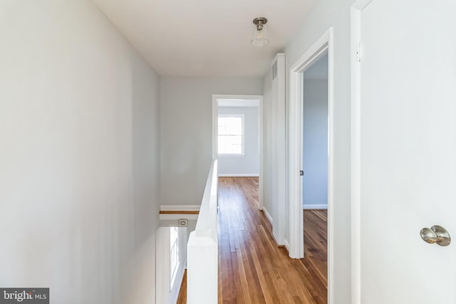 corridor with light wood-style floors, baseboards, and an upstairs landing