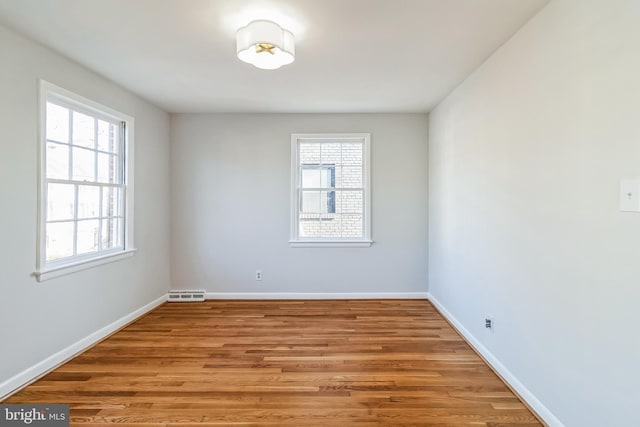 empty room with visible vents, wood finished floors, a wealth of natural light, and baseboards