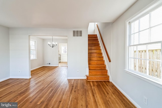 unfurnished living room featuring stairway, wood finished floors, visible vents, and baseboards