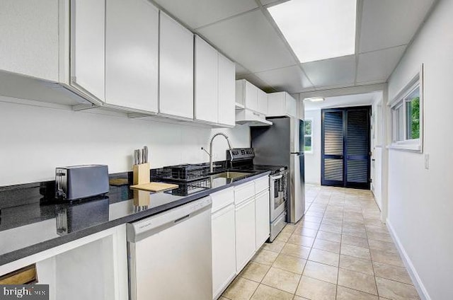 kitchen with white cabinets, a paneled ceiling, light tile patterned floors, and stainless steel appliances