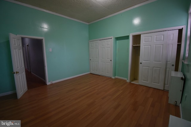 unfurnished bedroom with multiple closets, ornamental molding, a textured ceiling, and hardwood / wood-style flooring