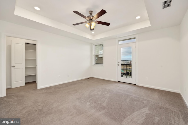 unfurnished bedroom featuring carpet, a raised ceiling, ceiling fan, a spacious closet, and a closet