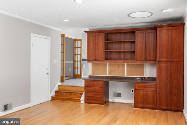 unfurnished office featuring built in desk, a textured ceiling, ornamental molding, and light hardwood / wood-style floors