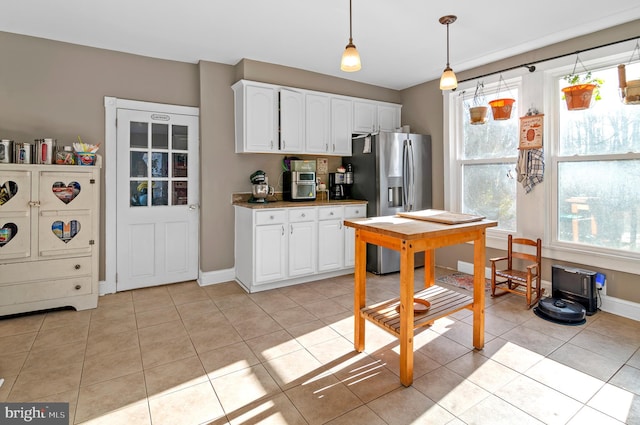 kitchen featuring hanging light fixtures, stainless steel fridge, stacked washing maching and dryer, light tile patterned floors, and white cabinetry