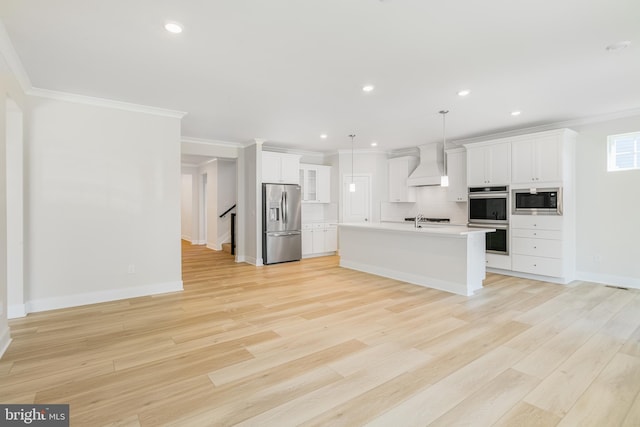 kitchen with a kitchen island with sink, premium range hood, hanging light fixtures, appliances with stainless steel finishes, and light hardwood / wood-style floors