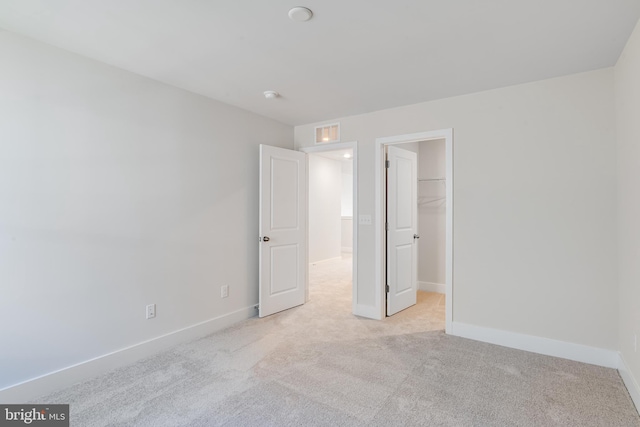 unfurnished bedroom featuring a walk in closet, light colored carpet, and a closet