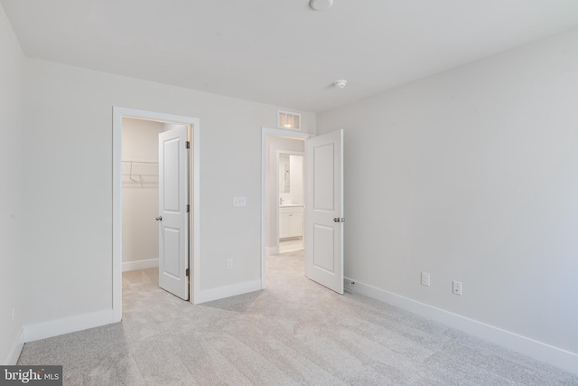 unfurnished bedroom featuring a walk in closet, a closet, and light colored carpet