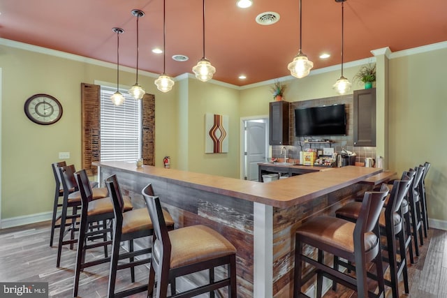 bar featuring tasteful backsplash, ornamental molding, hanging light fixtures, and hardwood / wood-style flooring