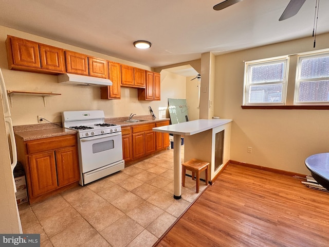 kitchen featuring sink, white gas range oven, light hardwood / wood-style flooring, ceiling fan, and a kitchen bar