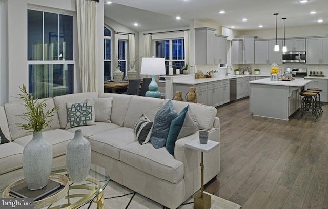 living room with vaulted ceiling, light hardwood / wood-style flooring, and sink