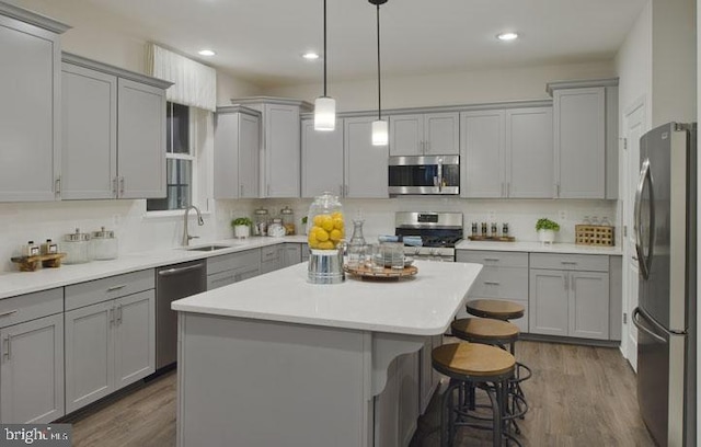 kitchen with appliances with stainless steel finishes, sink, gray cabinets, a kitchen island, and dark hardwood / wood-style floors